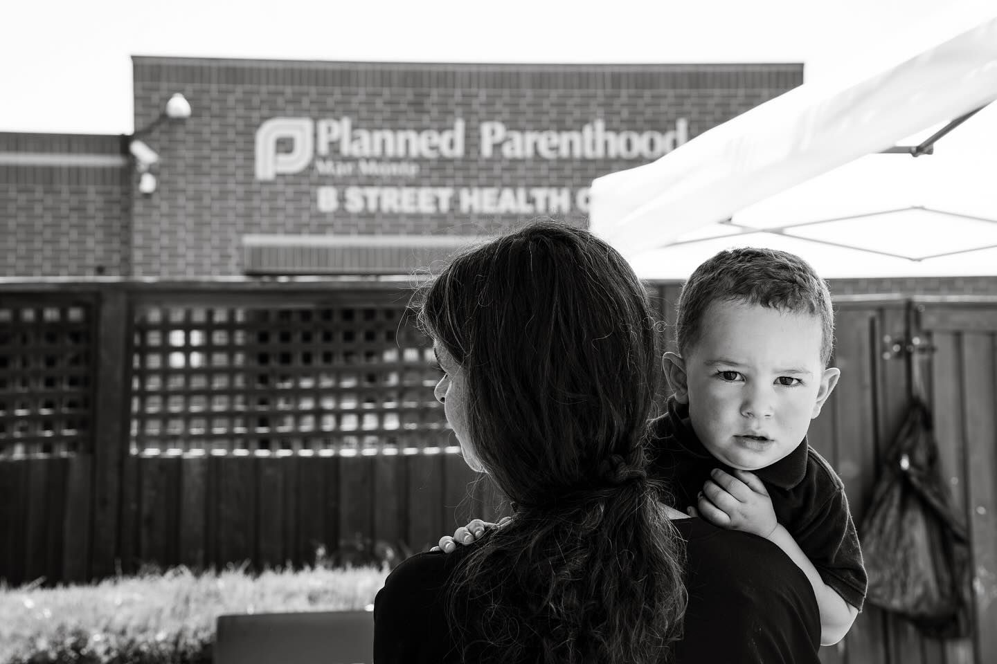 A mother holds her young son on her shoulder outside the Planned Parenthood B Street Health Center; the boy looks back at the camera.