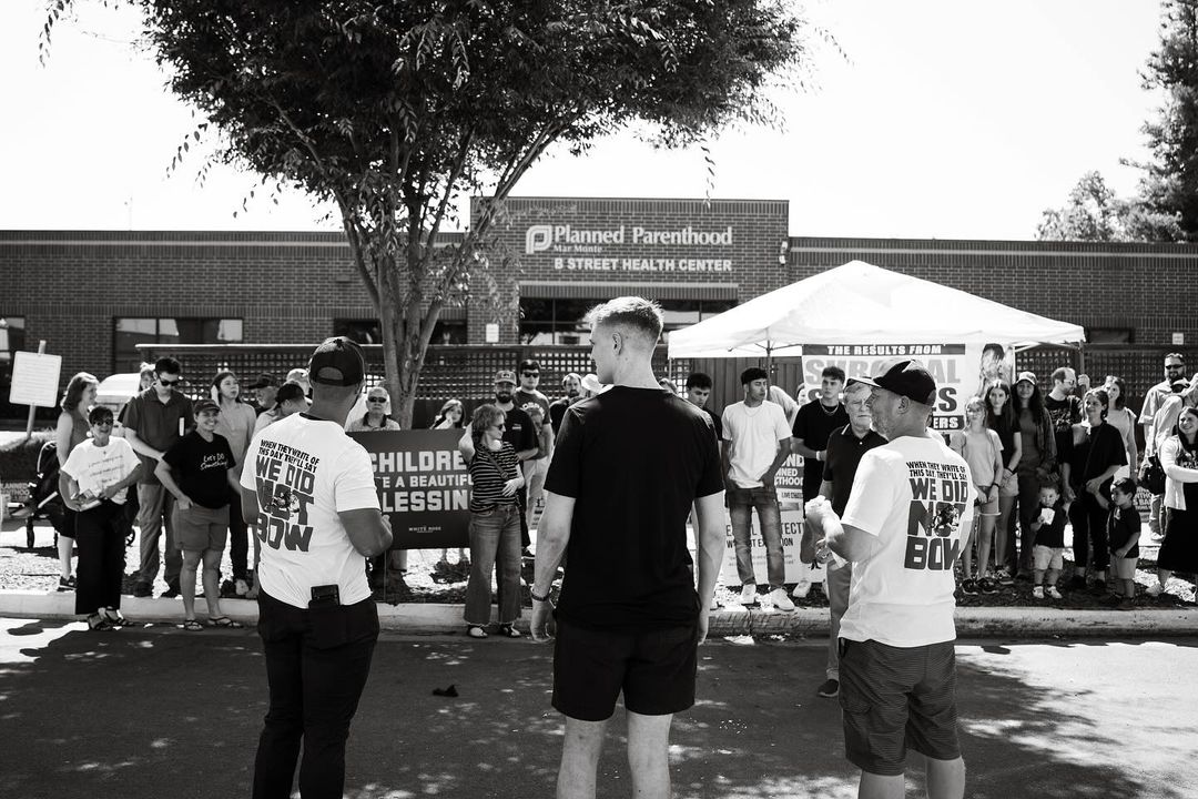 Two advocates in 'We Did Not Bow' shirts leading supporters gathered outside Planned Parenthood.